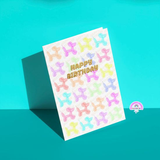 The Balloon Dog Birthday Card by My Store displays pastel balloon animals in a grid with Happy Birthday scripted in gold. It stands out charmingly against a turquoise background, perfect for celebrating a special day.