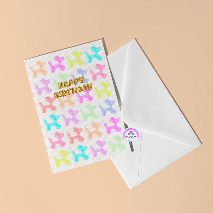 My Stores Balloon Dog Birthday Card features colorful balloon animal patterns and Happy Birthday text on the front, accompanied by a white envelope on a beige background—ideal for celebrating that special day.