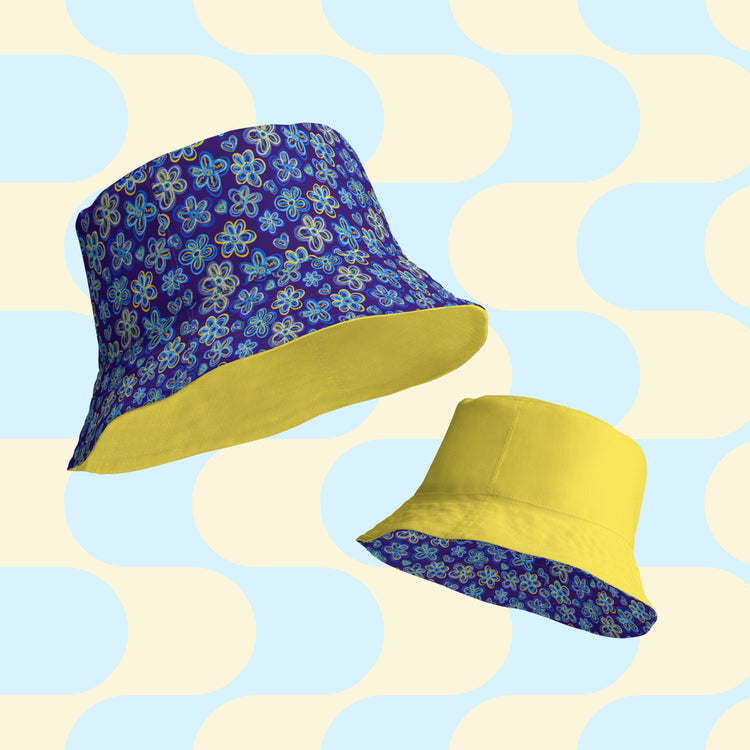 The Bloomscape Reversible Bucket Hat by My Favourite Colour is Rainbow features two designs: a blue floral pattern and solid yellow. Crafted from breathable fabric, these bucket hats are ideal as a streetwear accessory.