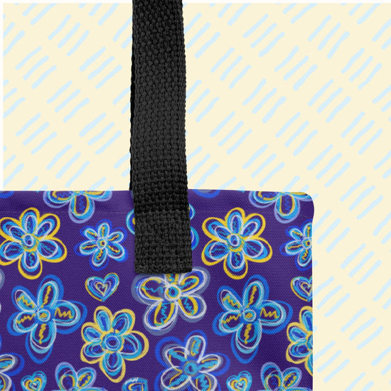 The Bloomscape Tote Bag by My Favourite Colour is Rainbow is a spacious tote bag featuring a vibrant flower pattern on a dark blue background, with black handles.