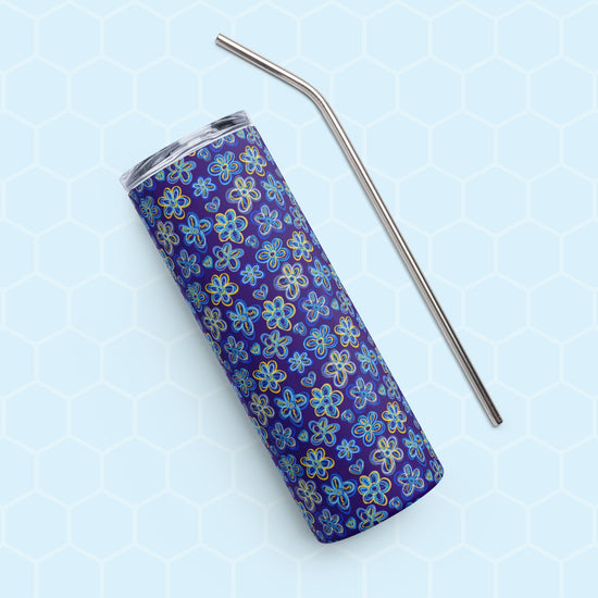 A Bloomscape Stainless Steel Tumbler by My Favourite Colour is Rainbow, featuring a design of large flowers and small hearts in shades of blue and yellow on a royal blue background shown on its side with a matching metal straw.