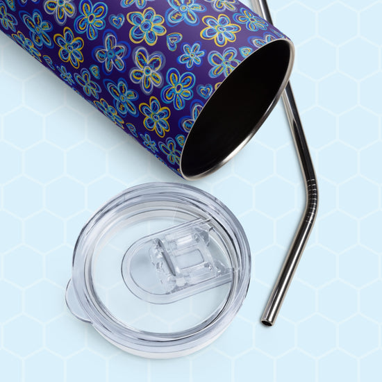 Close-up of a Bloomscape Stainless Steel Tumbler by My Favourite Colour is Rainbow, featuring a blue floral design. It lies on its side with a clear lid and metal straw.