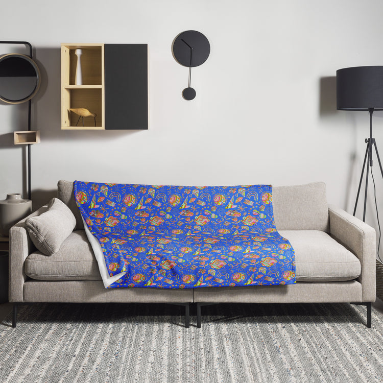 A modern, cosy living room showcases a light grey sofa with a My Favourite Colour is Rainbow Blue Summer Sorbet Throw Blanket and a sleek black floor lamp. A round black wall clock and geometric shelves add character above, while a textured rug grounds the vibrant design.
