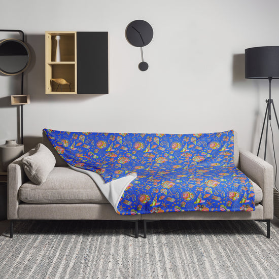 A gray sofa is adorned with My Favourite Colour is Rainbows Blue Summer Sorbet Throw Blanket, flaunting a vibrant floral design. The room features a modern clock, black floor lamp, circular mirror, wooden shelf with decor, and a textured gray rug enhancing the cozy atmosphere.