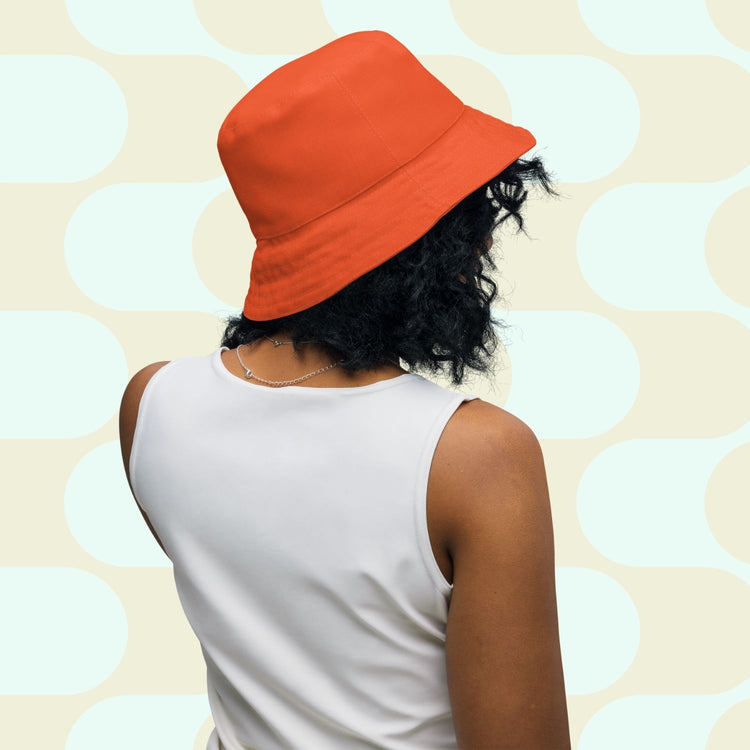 A person with curly hair wears the orange side of the Colour Block Reversible Bucket Hat by My Favourite Colour is Rainbow, facing away.