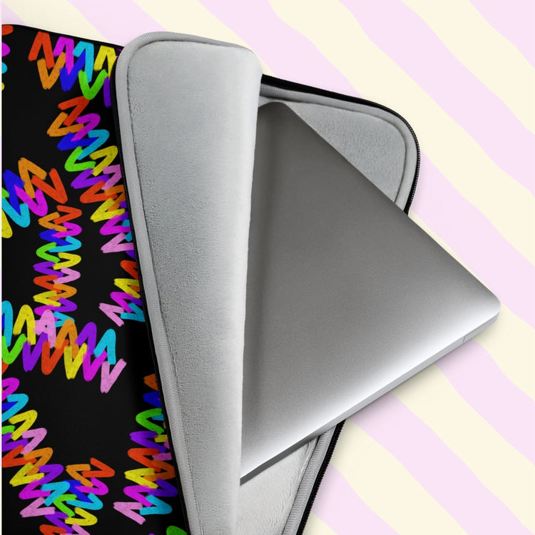 An Electric Zigzag Laptop Sleeve by My Favourite Colour is Rainbow, featuring vibrant red, yellow, blue, pink, and green zigzags on a black backdrop, encases a silver laptop.