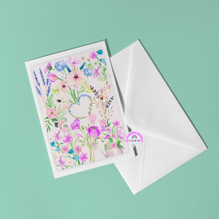 The Floral Watercolour Love Greeting Card from My Store features vibrant floral illustrations framing a white heart on mint green. Accompanied by an open white envelope, it showcases a flap sealed with a cheerful rainbow sticker.