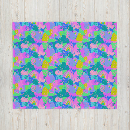 The Funfetti Throw Blanket by My Favourite Colour is Rainbow features a colorful, abstract pattern of hand-drawn shapes like fish, snails, and rainbows. It bursts with pink, purple, blue, and green hues on a light wooden background to add coziness to any space.