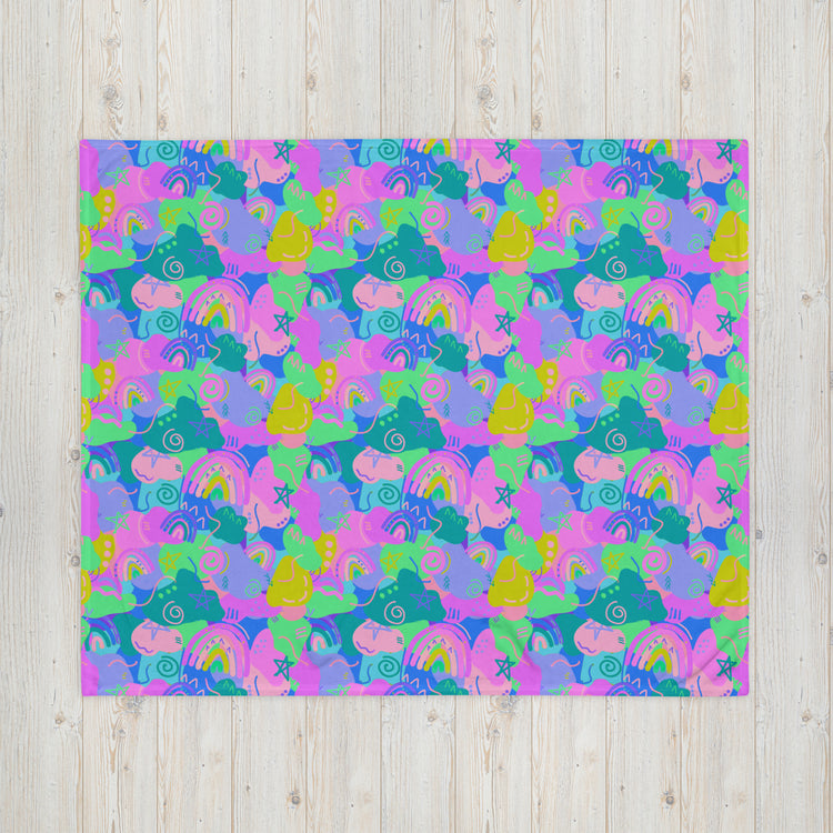 The Funfetti Throw Blanket by My Favourite Colour is Rainbow features a colorful, abstract pattern of hand-drawn shapes like fish, snails, and rainbows. It bursts with pink, purple, blue, and green hues on a light wooden background to add coziness to any space.
