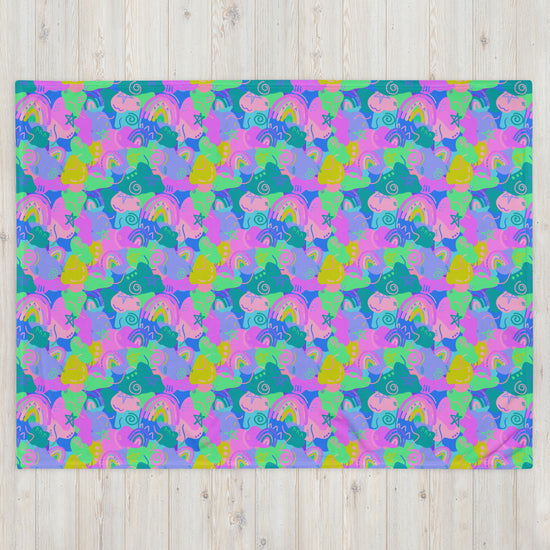 The Funfetti Throw Blanket by My Favourite Colour is Rainbow features a colorful abstract pattern with overlapping pink, purple, green, and blue shapes. Stylized birds, flowers, and swirls evoke a cozy and whimsical vibe. The vibrant design contrasts beautifully with the wooden texture background.