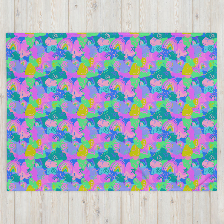 The Funfetti Throw Blanket by My Favourite Colour is Rainbow features a colorful abstract pattern with overlapping pink, purple, green, and blue shapes. Stylized birds, flowers, and swirls evoke a cozy and whimsical vibe. The vibrant design contrasts beautifully with the wooden texture background.