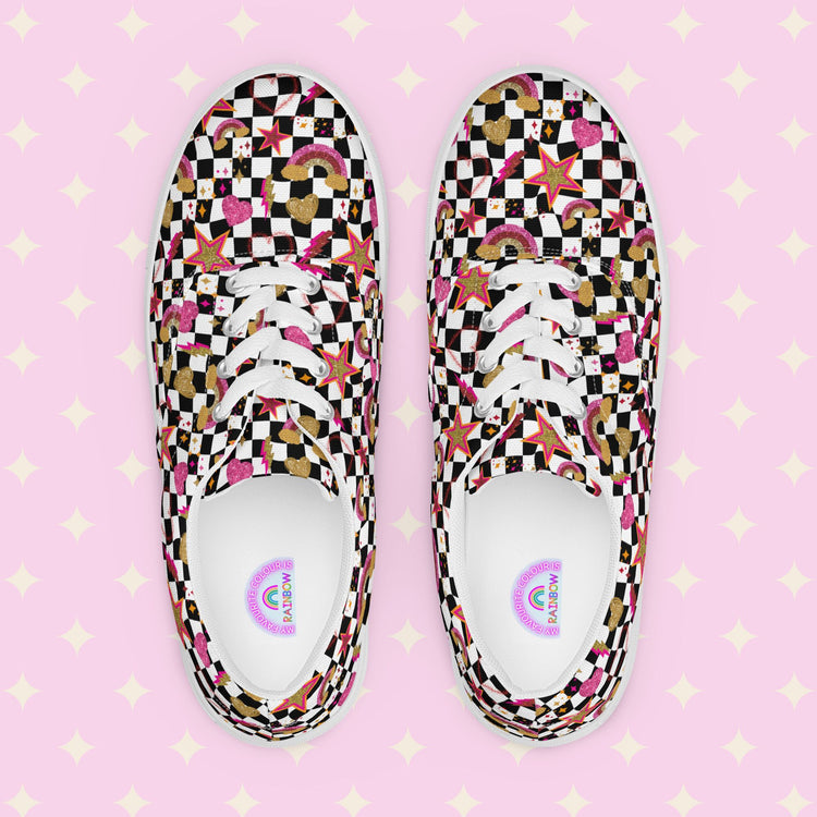 The Galaxy Canvas Sneakers by My Favourite Colour is Rainbow are decorated with a black and white checkerboard pattern, featuring gold, pink and red stars, hearts and rainbows. The inside of the shoes are white with My Favourite Colour is Rainbow branding on the footbed.  The shoes are shown on a pink background.