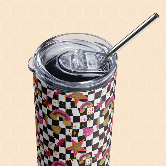 The Galaxy Stainless Steel Tumbler by My Favourite Colour is Rainbow is shown against a honeycomb-patterned background. It comes with a metal straw and clear lid, featuring a colorful design of rainbows, stars, and hearts over a black and white checkered pattern.