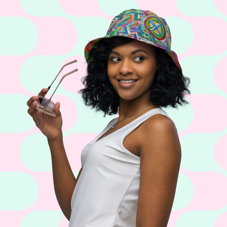 A woman in a white tank top holds pink sunglasses, wearing My Favourite Colour is Rainbows Geometric Rainbow/Love in Neon Reversible Bucket Hat, against a pastel polka dot backdrop that echoes peace and love.