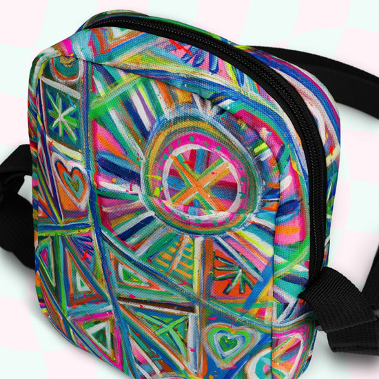 The Geometric Rainbow Mini Crossbody Bag by My Favourite Colour is Rainbow showcases a vivid mix of triangles, circles, and hearts in bright blue, pink, green, and orange hues. It features black adjustable straps and a secure zipper closure.