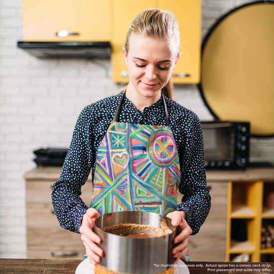 A person in a polka dot shirt and a Geometric Rainbow Apron by My Favourite Colour is Rainbow holds a round cake mold on a wooden countertop. The kitchen, with yellow cabinets and a brick backsplash, sets the perfect backdrop, while appliances are neatly arranged in the background.  The apron features vivid geometric designs in blue, pink, and green