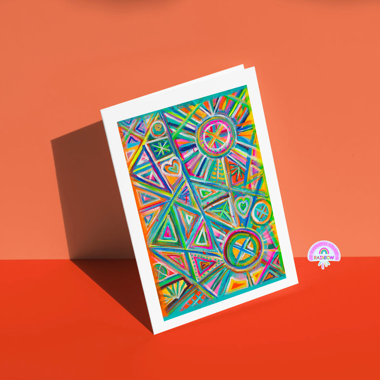 The Geometric Rainbow Greeting Card by My Store features colorful geometric patterns of triangles, circles, and hearts in vivid blues, pinks, and oranges. Its displayed on an orange surface against a matching background with a small geometric rainbow sticker.