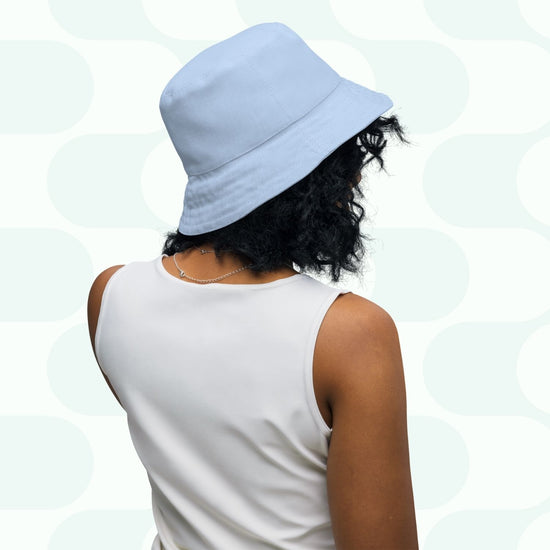 A person with curly hair wears the Green Rainbow Reversible Bucket Hat from My Favourite Colour is Rainbow and a white sleeveless top, shown from behind against a stylish patterned backdrop—ideal for fans of versatile fashion in various sizes.