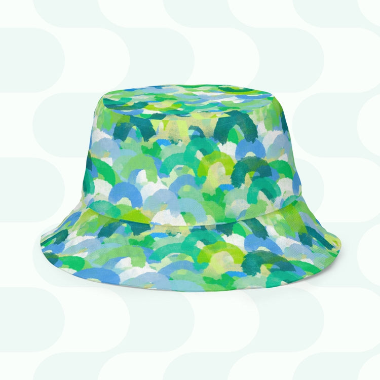 The Green Rainbow Reversible Bucket Hat by My Favourite Colour is Rainbow, available in various sizes, showcases a vibrant green, blue, and white semicircle pattern on a light backdrop with a delicate circular design. Style BFF approved for your next outing!.