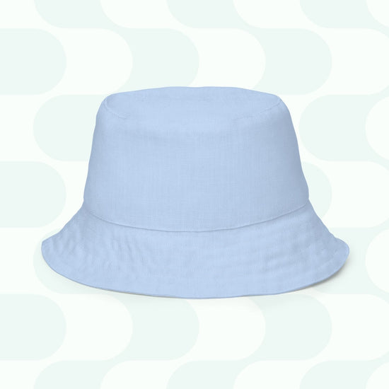 The Green Rainbow Reversible Bucket Hat from My Favourite Colour is Rainbow rests on a patterned background with light gray and white geometric shapes. Perfect for any occasion, this stylish accessory is your new Style BFF, available in multiple sizes for the ideal fit.