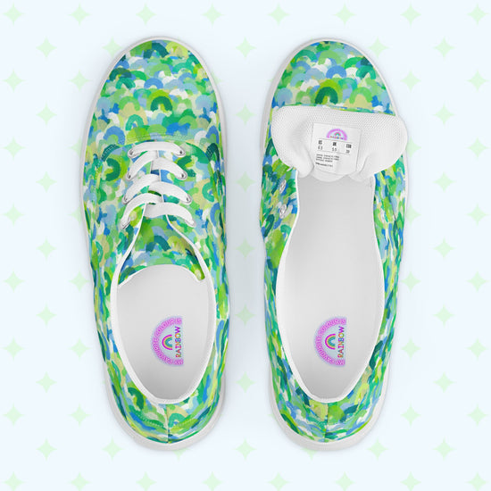 The Green Rainbow Canvas Sneakers from My Favourite Colour is Rainbow feature a vibrant green and blue rainbow pattern. One shoe reveals the size label on the underside of the tongue.  The inside of the shoe is white with My Favourite Colour is Rainbow branding on the footbed.