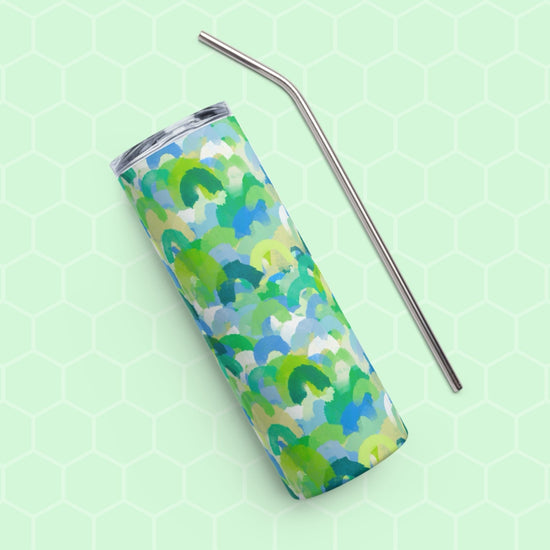 The Green Rainbow Stainless Steel Tumbler by My Favourite Colour is Rainbow, featuring a vibrant green, blue, and light blue abstract pattern with a metal straw, sits on a light green hexagon-patterned background.