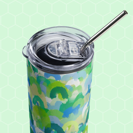 The Green Rainbow Stainless Steel Tumbler by My Favourite Colour is Rainbow features a blue and green abstract design, clear lid, and metal straw set against a light green hexagonal patterned background.