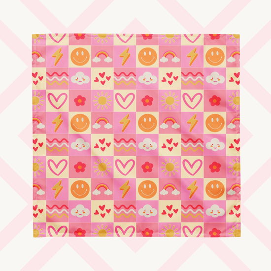 The Happy Smiles Sunny Days Bandana by My Favourite Colour is Rainbow features a vibrant pattern of smiley faces, lightning bolts, hearts, clouds, flowers, and waves on a pink and cream checkered background.