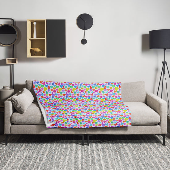 A modern living room showcases a beige sofa with My Favourite Colour is Rainbows Heart Attack Throw Blanket draped over it for a vibrant touch. A minimalistic black clock and cube shelf decorate the wall, with a black floor lamp to the right, set on a textured gray rug for warmth and style.