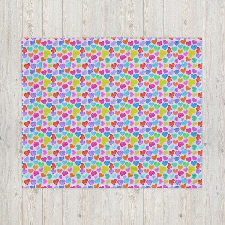 The Heart Attack Throw Blanket by My Favourite Colour is Rainbow features a lively multicolored heart design in pink, blue, green, orange, and purple on a light background, adding charm and character to the light wood floor.