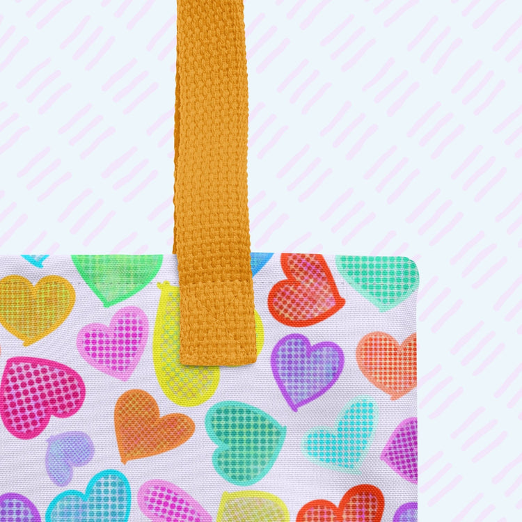 A close-up of the Heart Attack Tote Bag by My Favourite Colour is Rainbow featuring the sturdy black strap.  The tote bag has a rainbow pattern of colourful hearts.