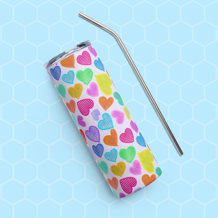 The Heart Attack Stainless Steel Tumbler by My Favourite Colour is Rainbow features multicolored hearts on white and rests elegantly on a blue hexagonal surface, accompanied by a sleek metal straw.