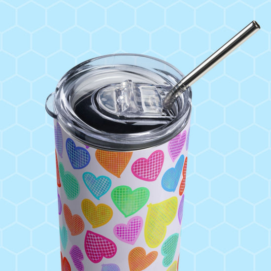 The Heart Attack Stainless Steel Tumbler by My Favourite Colour is Rainbow features a transparent lid, metal straw, and colorful patterned hearts on a pastel blue hexagonal background.