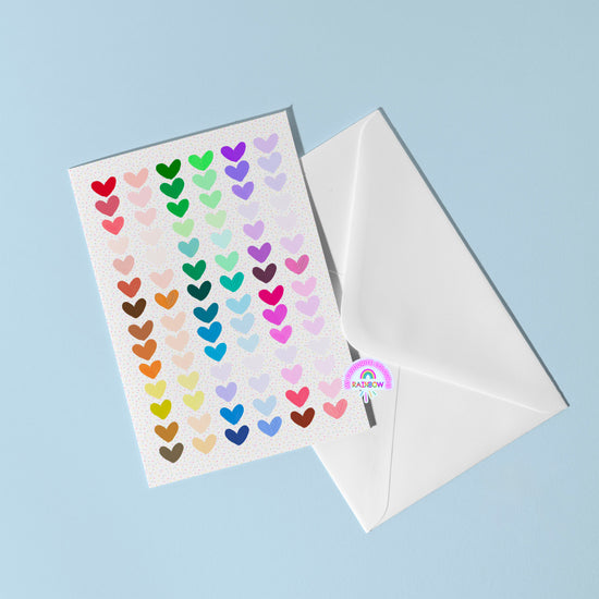 The Heart Attack Greeting Card by My Store features rows of colorful heart stickers on a bright card, set atop an open white envelope against a light blue background, with a charming round Rainbow sticker peeking from the edge.