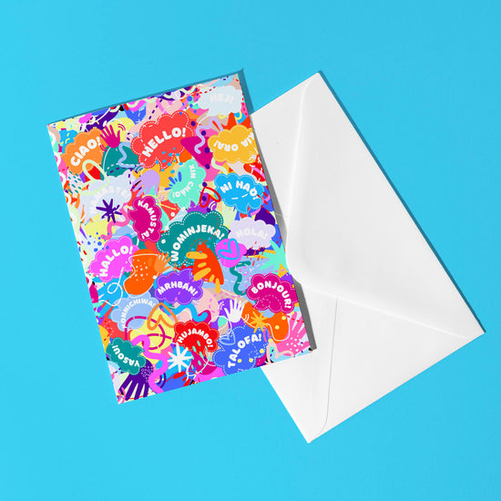 The Hello! Wominjeka! Greeting Card by My Store features a bold design with vibrant hand motifs and greetings like Hola, Bonjour, and Ciao on a blue background, paired with a white envelope, perfect for brightening someones day.