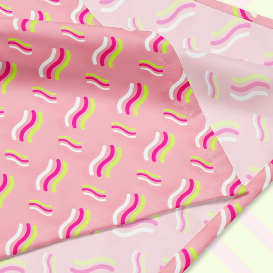A closeup of the 'Iced Vovo' Bandana by My Favourite Colour is Rainbow featuring a pink background with white, hot pink and lime green wavy lines suggestive of the iconic Iced Vovo biscuit. The design is printed on only one side of the bandana.