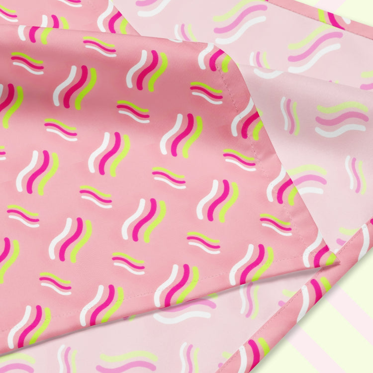 A closeup of the 'Iced Vovo' Bandana by My Favourite Colour is Rainbow featuring a pink background with white, hot pink and lime green wavy lines suggestive of the iconic Iced Vovo biscuit. The design is printed on only one side of the bandana.