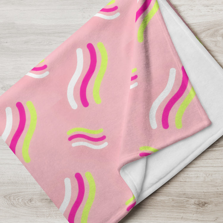 The Iced Vovo Throw Blanket by My Favourite Colour is Rainbow, featuring vibrant curved lines in white, lime green, and magenta, is draped over a light wooden surface to add a cozy touch to the room.