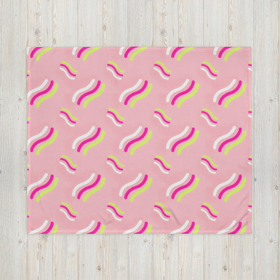 The Iced Vovo Throw Blanket by My Favourite Colour is Rainbow, featuring vibrant wavy lines in pink, white, yellow, and green, adds a lively and playful appearance when spread on a light wooden floor.
