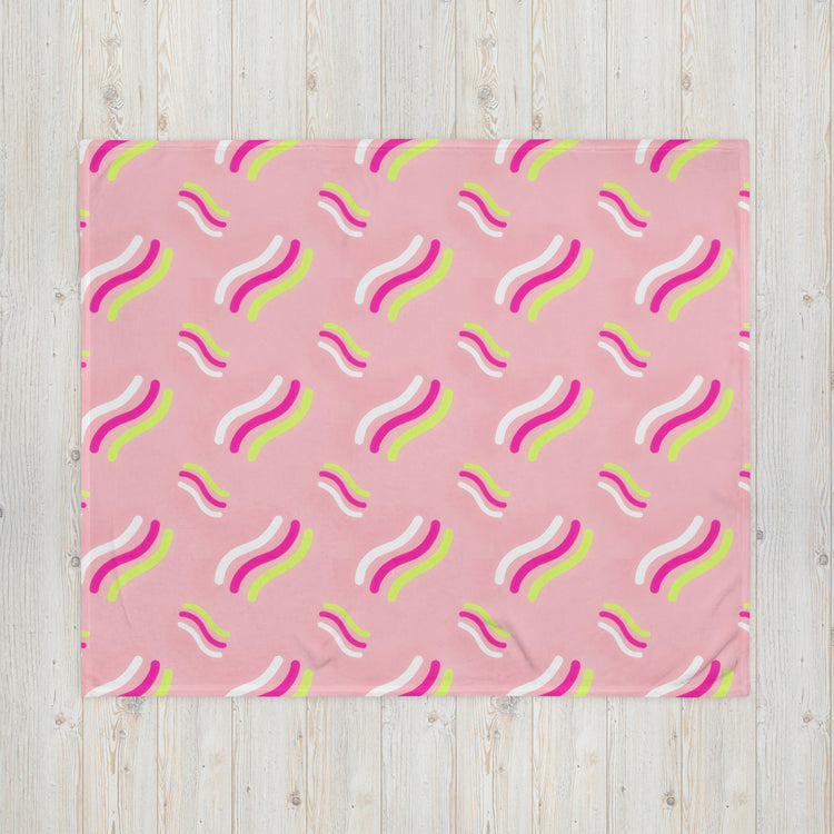 The Iced Vovo Throw Blanket by My Favourite Colour is Rainbow, featuring vibrant wavy lines in pink, white, yellow, and green, adds a lively and playful appearance when spread on a light wooden floor.