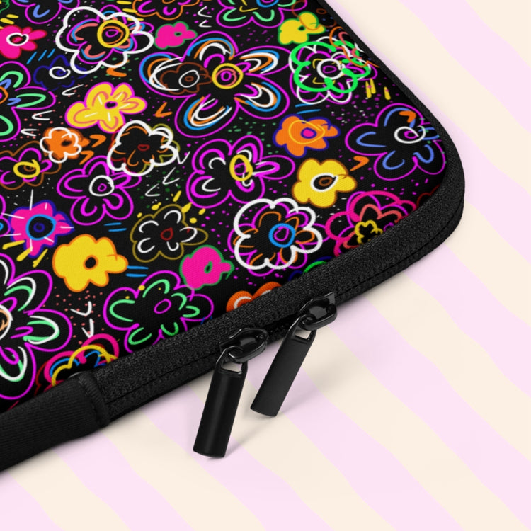 In the Midnight Garden Laptop Sleeve by My Favourite Colour is Rainbow showcases vibrant multicoloured flowers on a black background. It includes padding, lining, and two black zipper pulls. Shown on a soft pink and yellow striped background.