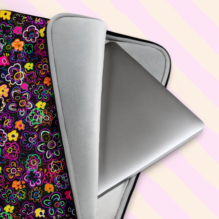 A silver laptop is shown partially out of the In the Midnight Garden Laptop Sleeve by My Favourite Colour is Rainbow. It features a colourful floral pattern, a black zipper and a soft grey padded interior. Shown on a pastel pink and yellow striped background.
