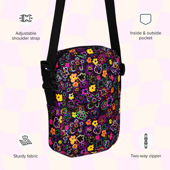 An infographic highlighting features of the In the Midnight Garden Mini Crossbody Bag by My Favourite Colour is Rainbow: adjustable shoulder strap, inside and outside pocket, sturdy canvas fabric and a two-way zipper.  The bag is decorated with a vibrant floral pattern with pink, orange, yellow, and green on a black background.