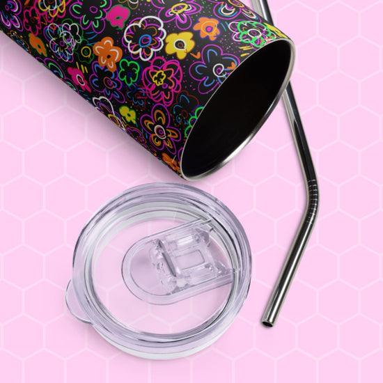 The In the Midnight Garden Stainless Steel Tumbler by My Favourite Colour is Rainbow sits on a pink hexagonal-patterned background, accompanied by a clear plastic lid and sleek metal straw, adding an eco-friendly touch to your drinkware collection with its colorful floral design.