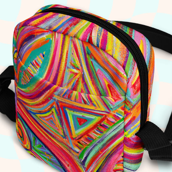 Discover the Karma Kaleidoscope Mini Crossbody Bag by My Favourite Colour is Rainbow, featuring a lively pattern of bold pink, orange, blue, and green swirls and geometric shapes. It is made of canvas-type material, has internal and external pockets and an adjustable black strap with a buckle on one side that can be extended to crossbody length.
