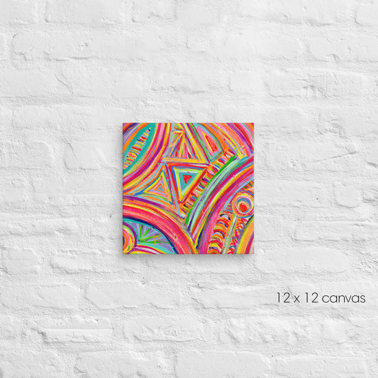 A vibrant 12x12 square canvas from My Favourite Colour is Rainbow named Karma Kaleidoscope showcases abstract patterns with swirling lines and geometric shapes in orange, blue, yellow, and green, mounted on a textured white brick wall.