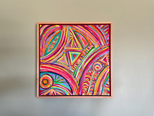 The Karma Kaleidoscope Framed Original Painting by My Store features vibrant swirls, triangles, and circles in pink, purple, orange, and yellow hues. Elegantly framed in simple wood, it is displayed on a plain light gray wall.
