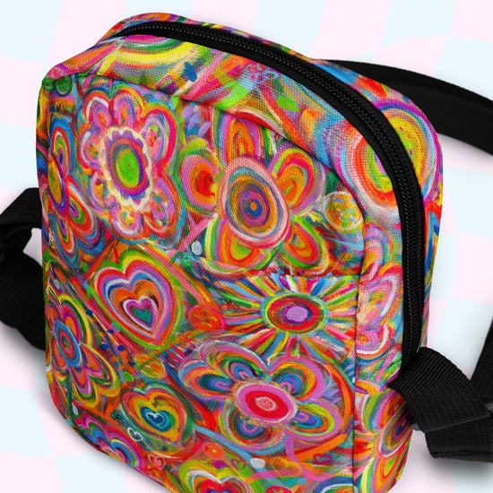 The Love in Neon Mini Crossbody Bag by My Favourite Colour is Rainbow showcases vibrant, swirling floral and heart designs in red, orange, green, blue, and yellow on a light teal and white checkerboard. With adjustable straps for comfort on any adventure.
