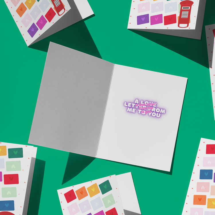 The Love Letter Valentines Card by My Store is open on a green background surrounded by similar cards. Inside, the text reads A love letter from me to you in pink. Each card features colorful envelope designs that bring rainbow joy to their covers.