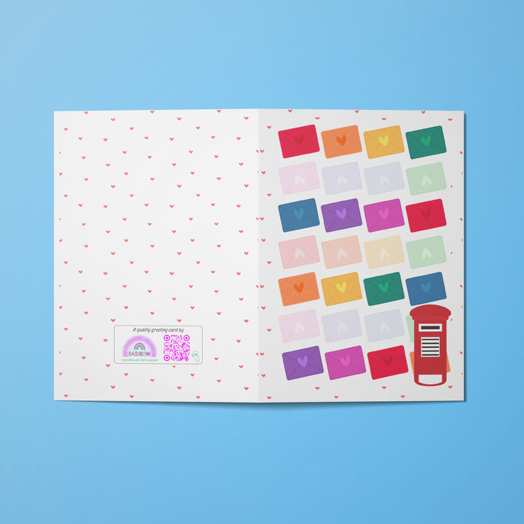 The Love Letter Valentines Card by My Store features an open design against a blue backdrop. The left side is decorated with red hearts, a QR code for rainbow joy, and text, while the right displays vibrant envelopes in rows next to a charming red British-style postbox.